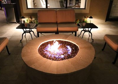 Outdoor patio with glowing fire pit, surrounded by cushioned seating and night lighting, creating a cozy ambiance.