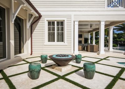 Modern patio with geometric tiles, fire pit, green planters, and outdoor seating near a pool.