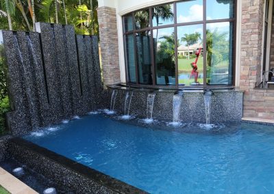 Luxurious backyard pool with elegant stone raise wall waterfall feature and tropical garden setting.