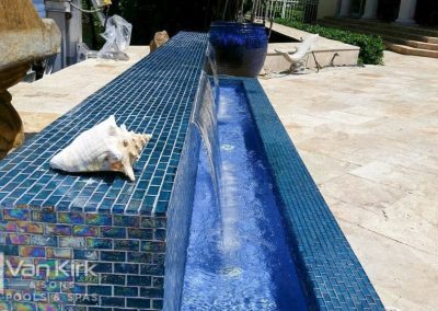 Luxurious pool raised wall with cascading water features and decorative shell on blue mosaic tile edge.