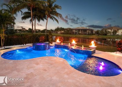 Luxurious backyard lagoon style freeform pool with a fire and water feature at sunset, surrounded by palm trees and modern homes.