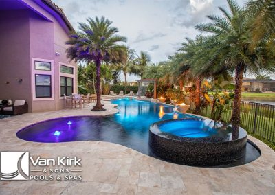 Luxurious backyard lagoon pool with palm trees and LED lighting at sunset.