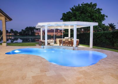 Luxurious backyard lagoon pool area with modern pergola at dusk, overlooking a serene lake and lush greenery.
