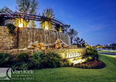 Grand stone waterfall feature with Riverstone signage surrounded by palm trees in Naples.