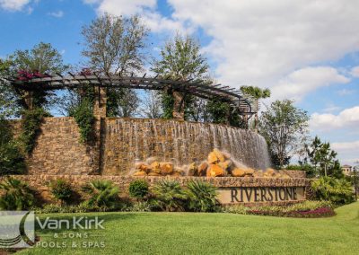 Scenic waterfall feature with greenery at Riverstone entrance, designed by Van Kirk & Sons Pools & Spas.
