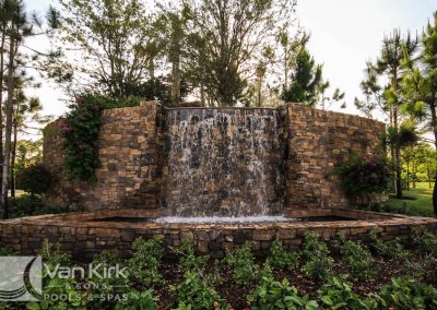 Rustic stone waterfall surrounded by lush greenery in a tranquil garden setting.
