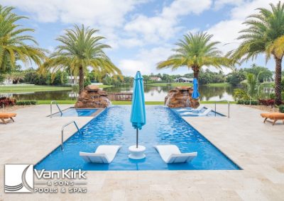 Luxury pool with loungers, umbrellas, and palm trees overlooking a serene lake view.