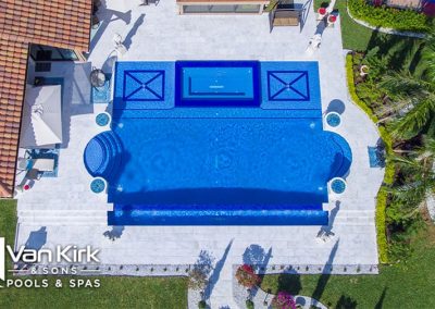Aerial view of luxury backyard roman style pool and spa area by Van Kirk & Sons surrounded by greenery and patio furniture.