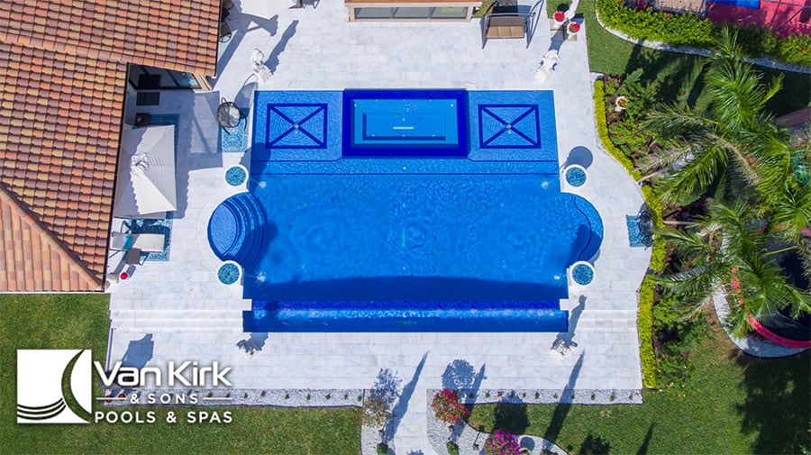 Luxurious backyard Roman style pool and spa oasis with modern design, surrounded by lush greenery and patio space.