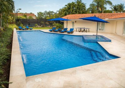 Luxurious backyard with a modern geometric shaped swimming pool, lounge chairs, and umbrellas under a clear sky.