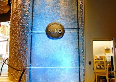 Luxurious indoor water feature with blue lighting and Kuro emblem by Van Kirk & Sons Pools & Spas.