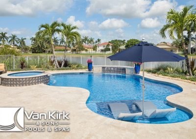 Luxurious backyard pool with spa and umbrella by Van Kirk & Sons, surrounded by palm trees and vibrant landscaping.