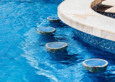 Swim up bar in a blue swimming pool with tiled edges for luxury outdoor design.