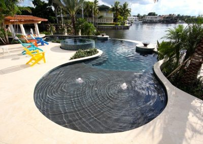 Luxurious infinity pool with colorful chairs and a serene waterfront view surrounded by lush greenery.