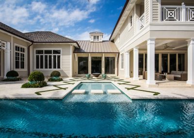 Luxury home with modern pool design, patio, and elegant landscaping under a clear blue sky. Pool steps that go across the pool.