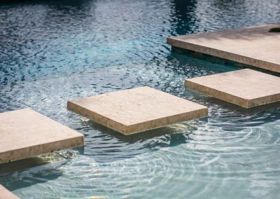 Stepping stones over clear, rippling blue pool water, creating a tranquil and inviting outdoor space.