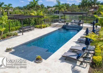 Luxurious outdoor straight line swimming pool with lounge chairs, palm trees, and pergola, by Van Kirk & Sons Pools & Spas.