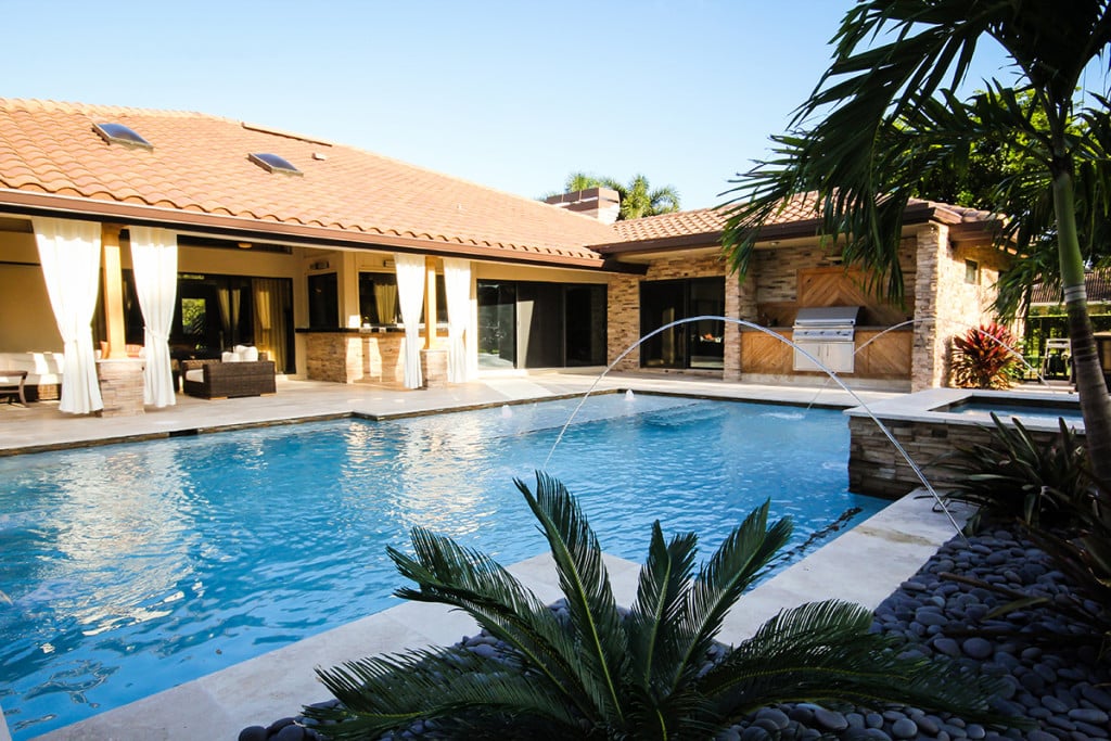 Luxurious home with pool, poolside seating, and tropical plants, perfect for outdoor relaxation and entertainment.
