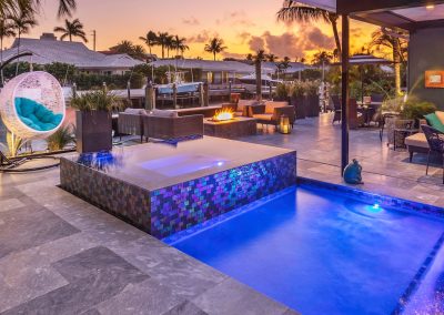 Luxurious modern patio with illuminated pool, a fire feature, cozy seating, and hanging chair at sunset. Ideal for relaxation.