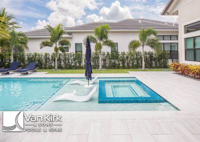 Luxury wet edge pool and spa area with loungers, palm trees, and blue sky at Van Kirk & Sons Pools & Spas.