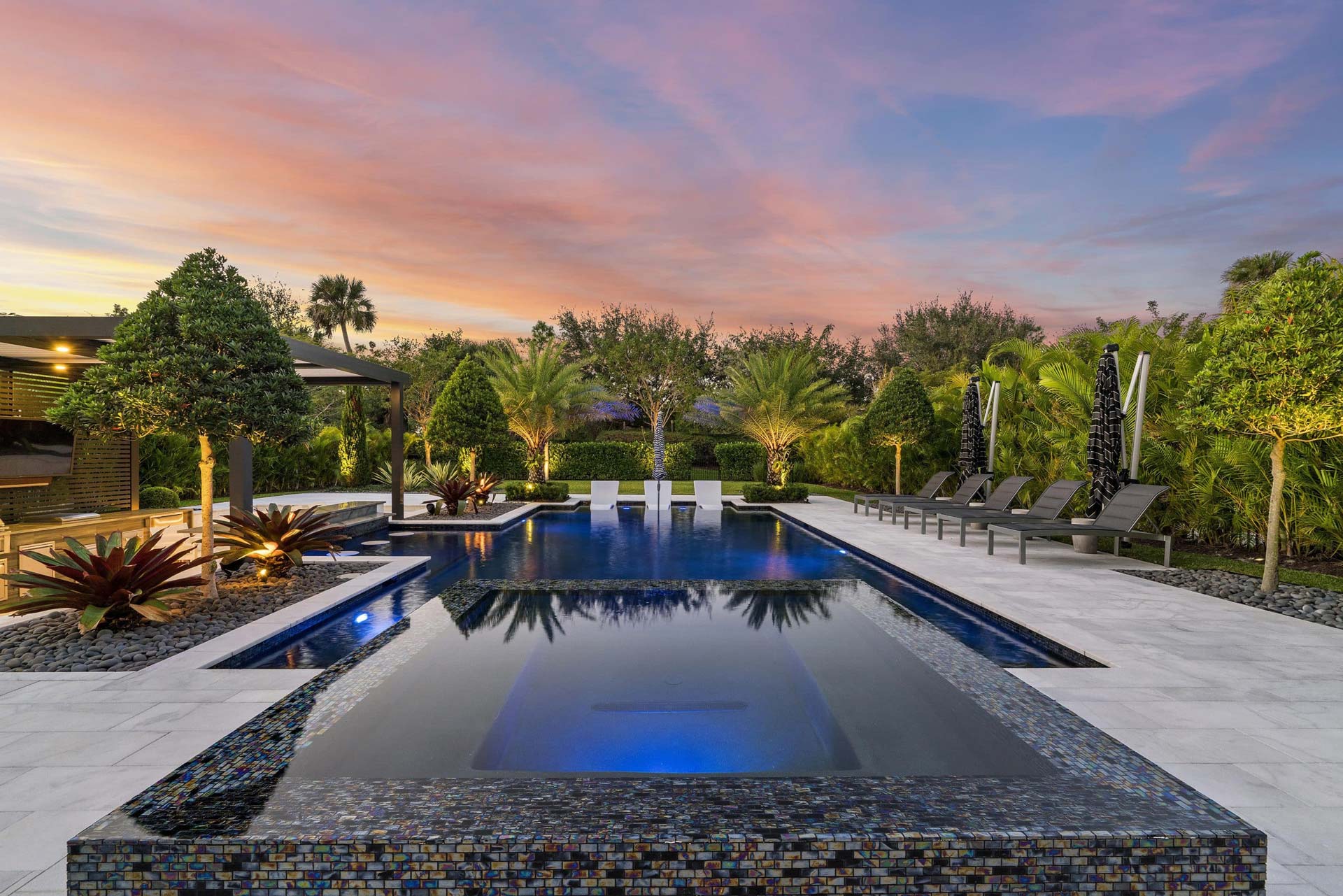 Luxurious outdoor pool area with seating and tropical landscaping at sunset in Boca Raton, Florida.