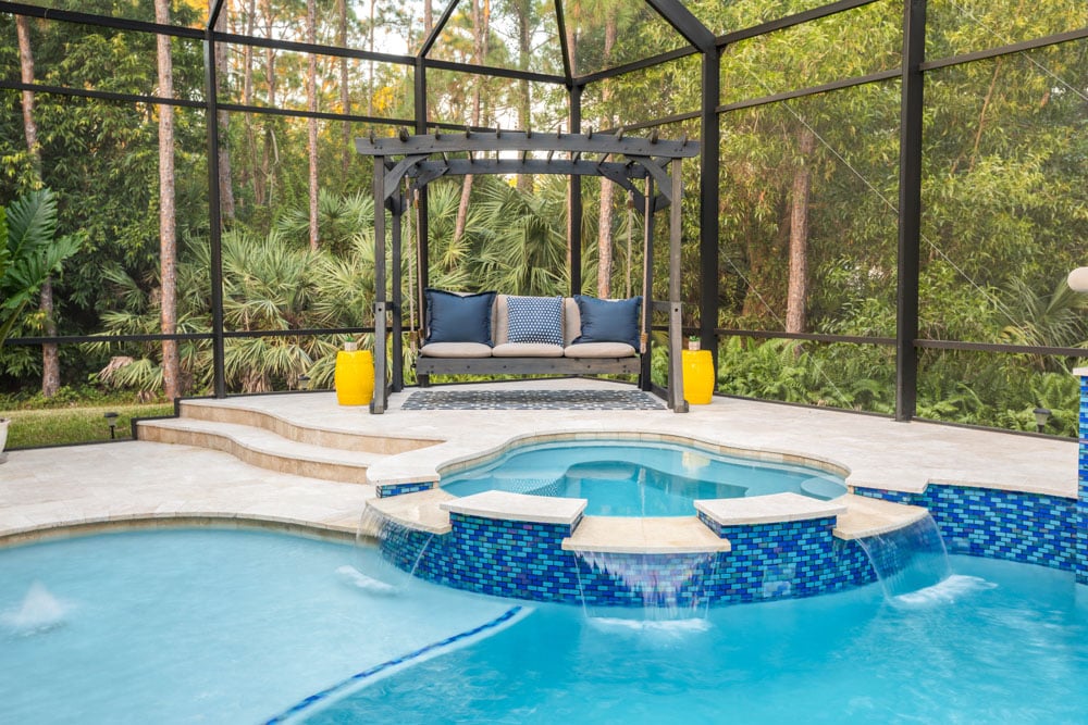 Luxurious outdoor pool area with modern pergola and swing seat, surrounded by lush greenery in naples florida