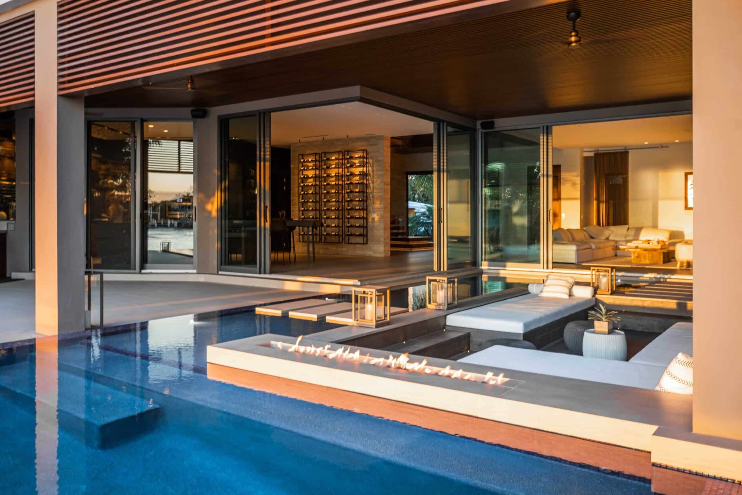 Modern luxury home with poolside lounge, fire pit, and indoor-outdoor living space at sunset in lotus palm
