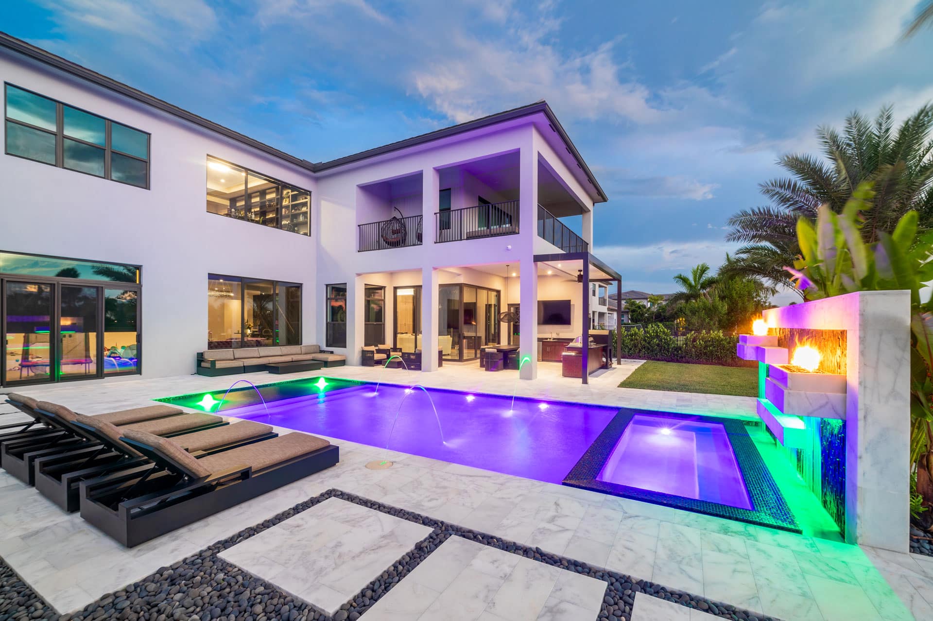 Luxury modern house with renovated pool, patio lounge, and fire features under a twilight sky.