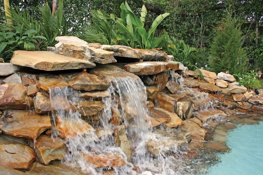 Rock waterfall flowing into a serene pool surrounded by lush greenery in hillsboro beach.