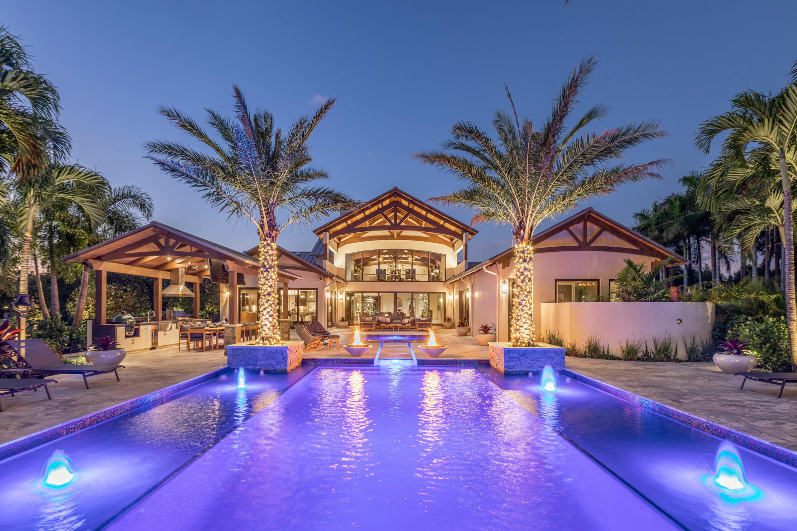 Luxury house in Deerfield Beach, FL with illuminated palm trees and pool at dusk, showcasing modern architecture and elegant outdoor lighting.