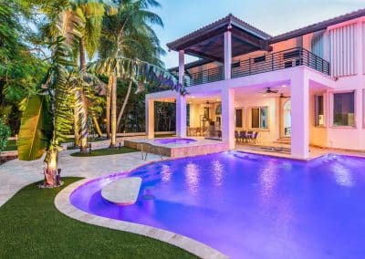 Van Kirk Pools designed this luxury Deerfield Beach backyard with a custom pool featuring vibrant purple LED lights and a raised spa.