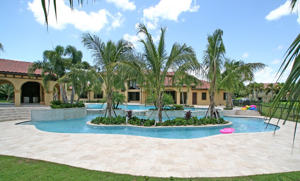 Luxury tropical pool with palm trees and inflatables at a resort under a blue sky.