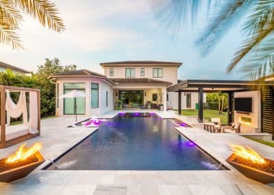 Van Kirk Pools built this modern South Florida pool with a raised spa, sun shelf with loungers, and two fire & water bowls.