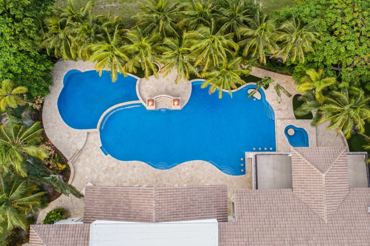 Aerial view of luxury tropical pool surrounded by palm trees and terrace, offering a relaxing getaway ambiance in Miami, FL.