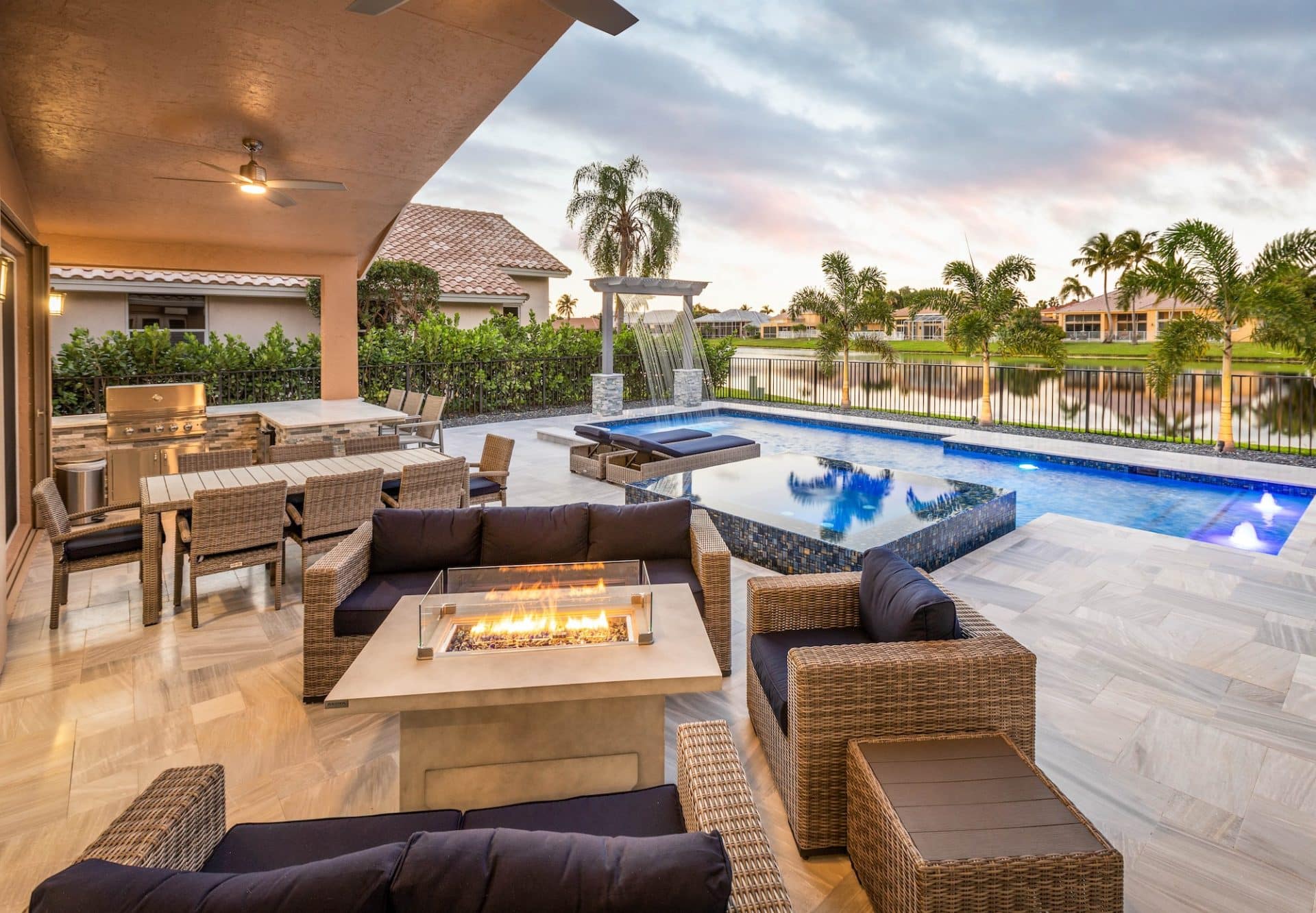 Luxurious outdoor patio with pool, cozy fireplace, and modern seating by the water at sunset.