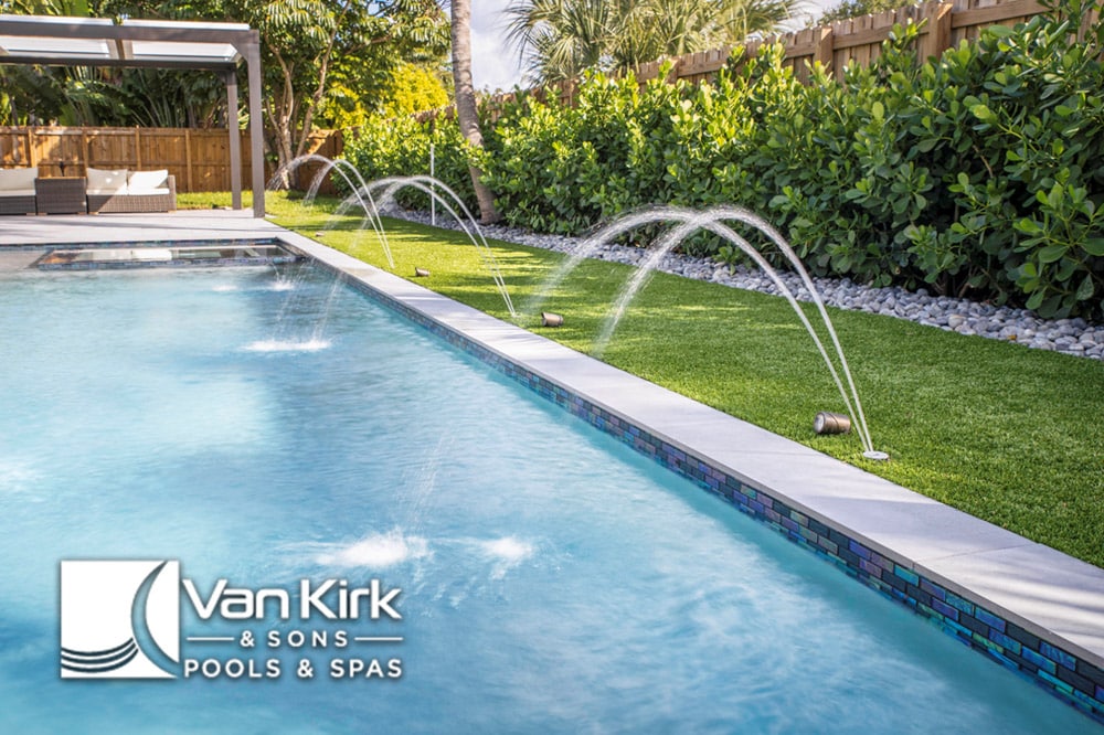 Modern pool with water jets and lush greenery in palm beach