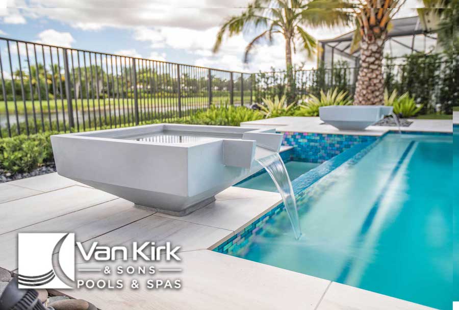 Luxurious modern pool at a home in Port St. Lucie, Florida with cascading water feature by Van Kirk & Sons Pools & Spas, surrounded by lush greenery.