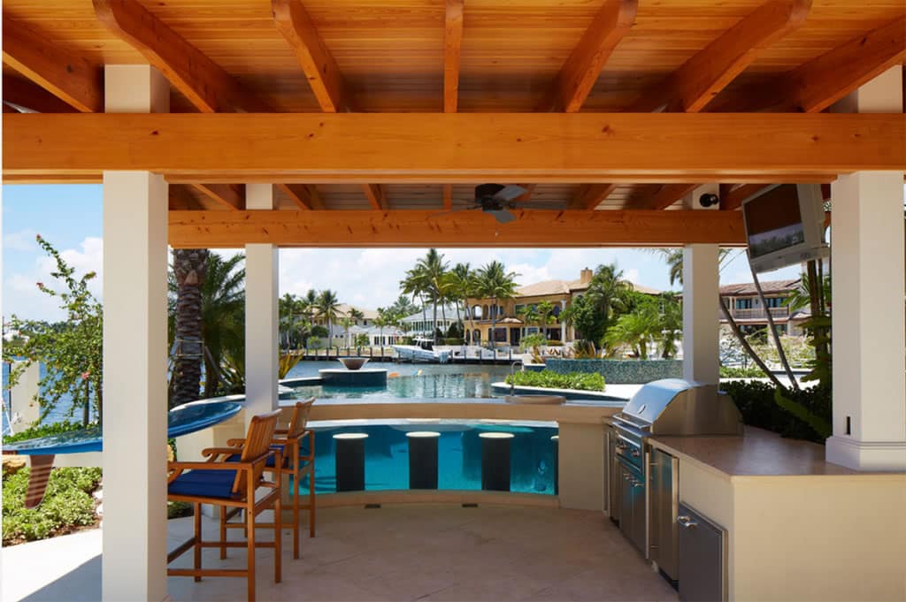 Luxurious outdoor kitchen with modern grill and bar seating overlooking a serene waterfront view with lush palm trees in lake worth