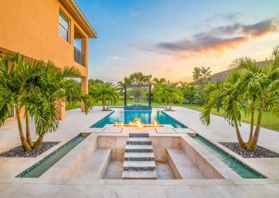 Van Kirk Pools built this modern pool in South Florida with a raised spa, a waterfall wall, and two large fire bowls.