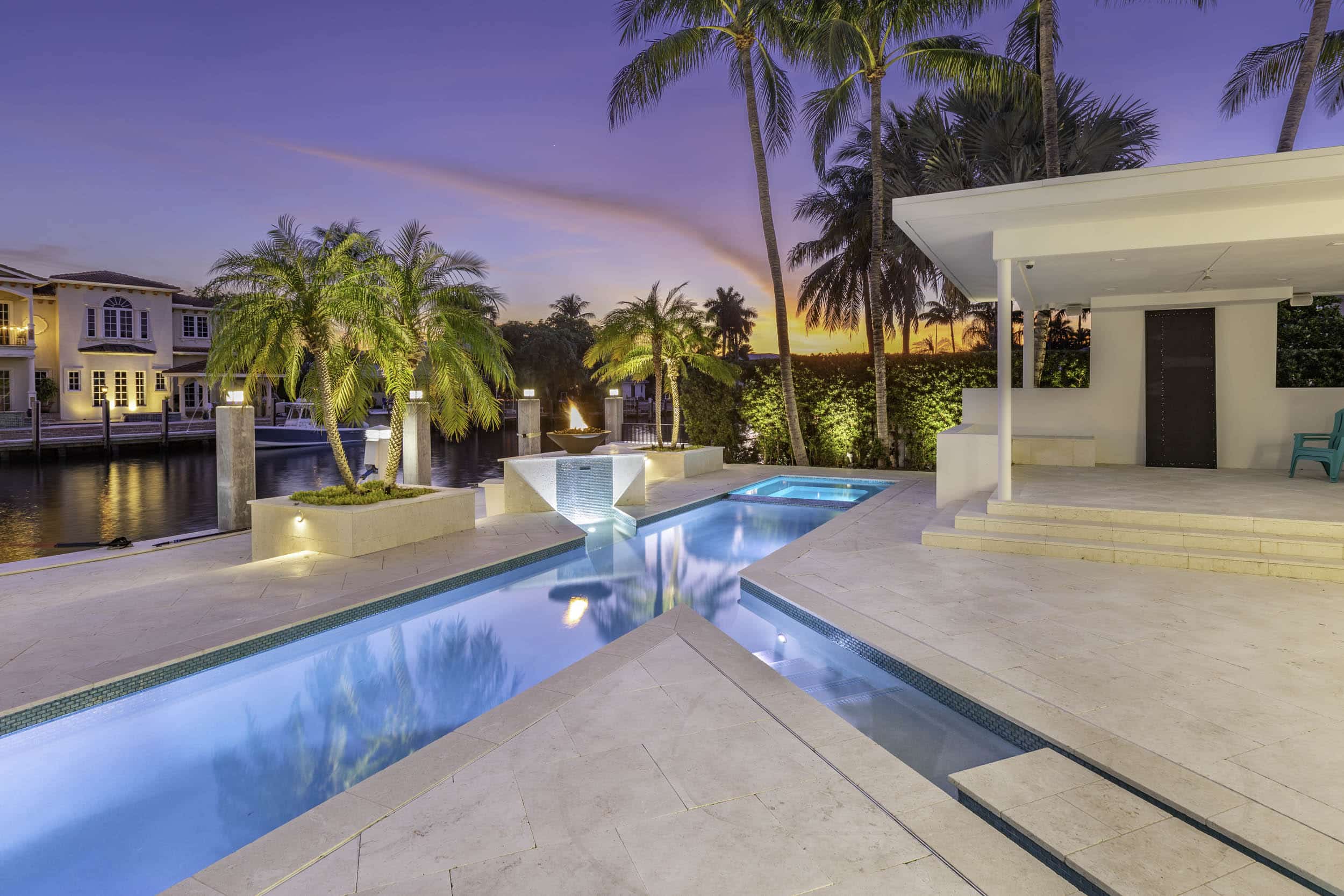 Luxurious poolside view with palm trees, waterfront backdrop, and sunset sky at a modern villa.