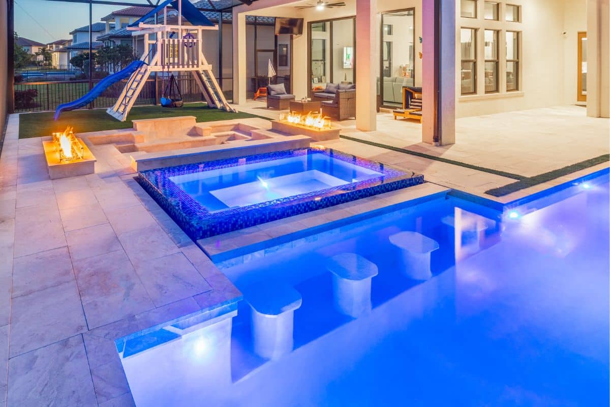 modern enclosed geometric pool with raised spa, built-in bar stools, and fire features.