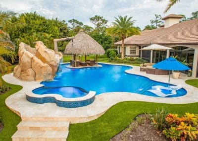 Free-form lagoon pool with rock slide, tiki hut, and sun shelf loungers.