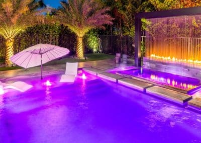 Night view of geometric pool with fire and water wall, sun shelf and LED lighting.