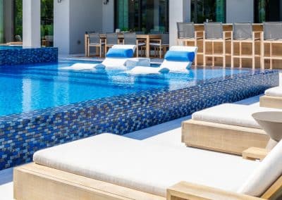 Infinity edge pool with tiled exterior and in-water loungers at luxury home.