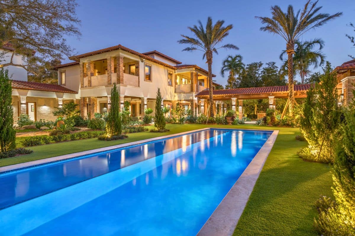 A long, lighted lap pool at a luxury Mediterranean estate in Palm Beach at twilight, with extensive landscape lighting.