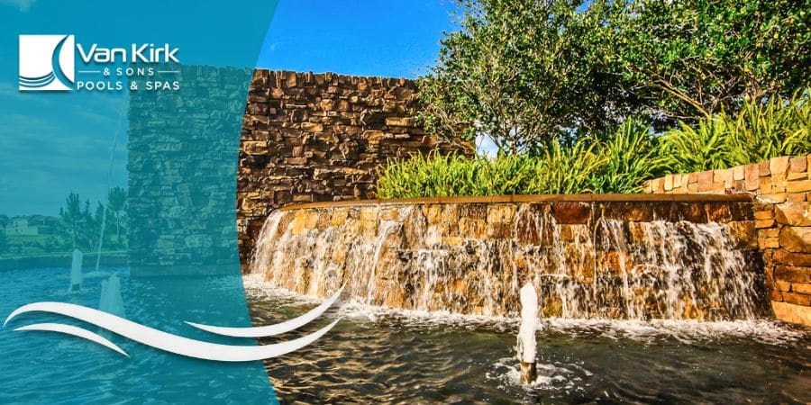 A large stacked stone community entrance feature with a wide waterfall and fountains, built by Van Kirk Pools in Naples.