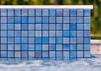 A close-up, water-level view of a raised spa wall finished with blue, iridescent glass mosaic tile.