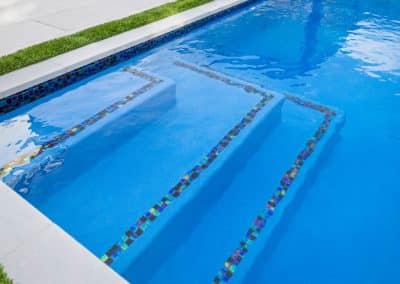 A close-up of custom pool entry steps outlined with iridescent mosaic tile in a modern pool with a blue interior.