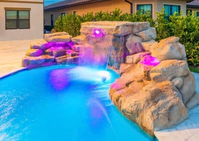 A custom-built rock grotto and waterfall on a freeform pool, illuminated with purple and blue color-changing LED lights.