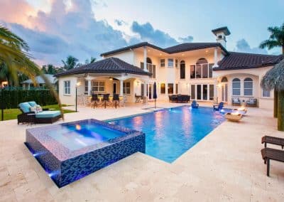 A luxury Parkland pool at dusk with a raised, lighted mosaic tile spa, a fire bowl, and a large outdoor kitchen.
